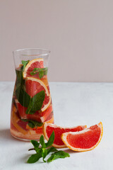 Glass jug of Cocktail grapefruit with fruits. fresh Grapefruit juice with green mint on beige background. grapefruit lemonade. Refreshing summer drinks. copy space.vertical.