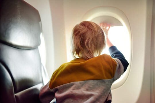 Little child traveling by an airplane. Preschooler boy looking at the aircraft window during the flight. Air travel with kids.