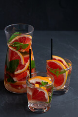 cocktail in glass.Cocktail grapefruit. glass Jug of Grapefruit lemonade with fresh fruits and green mint in a glass on black background. copy space. Refreshing summer drinks on the table.vertical