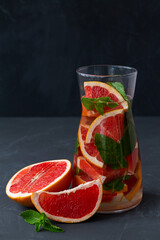 Cocktail grapefruit. glass Jug of Grapefruit lemonade with fresh fruits and green mint in a glass on black background. copy space. Refreshing summer drinks on the table.vertical