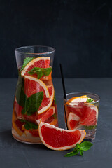 juice in a glass on black.Cocktail grapefruit. glass Jug of Grapefruit lemonade with fresh fruits and green mint in a glass on black background. copy space. Refreshing summer drinks on the table.
