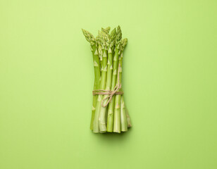 bunch of fresh raw asparagus on green paper background, top view