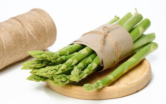 A Bunch Of Fresh Asparagus Wrapped In Brown Paper Lies In A Wooden Plate