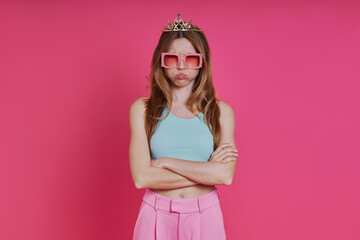 Displeased woman in funky crown showing her thumb down while standing against pink background