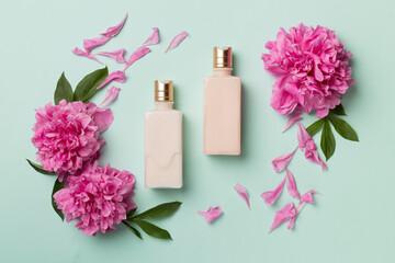 Flat lay composition with cosmetic bottles and peony flowers on on color background, top view