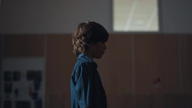 Upset schoolboy walking empty campus corridor alone. Thoughtful kid going hall