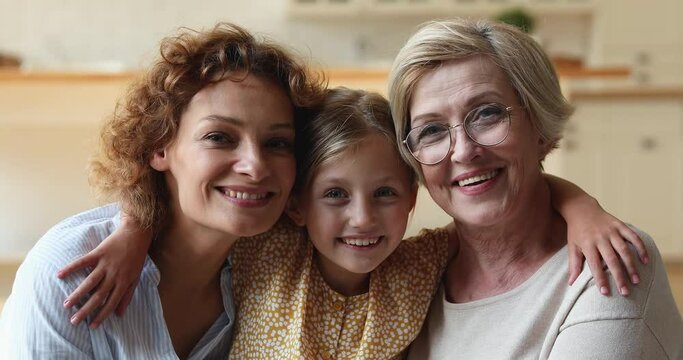 Portrait of sincere happy three different female generations family looking at camera, showing strong good relations, adorable little child girl embracing beautiful mother and caring older granny.