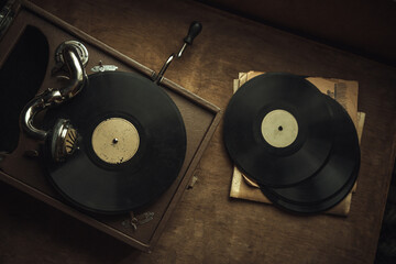 Vintage record player on the table in retro style. A square gramophone with a wind-up handle on the table.Black records with music.