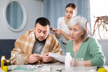 Elderly mother and a young wife give pills and medicines to her husband during his illness