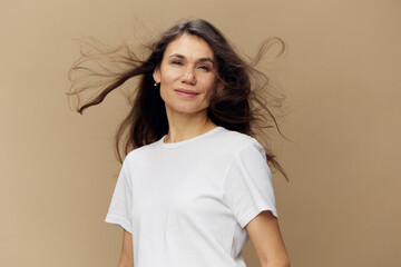 portrait of a sweet, beautiful, charming, pleasant woman with black hair developing in the wind, in a white clean t-shirt smiling pleasantly at the camera. Studio photo on a plain background