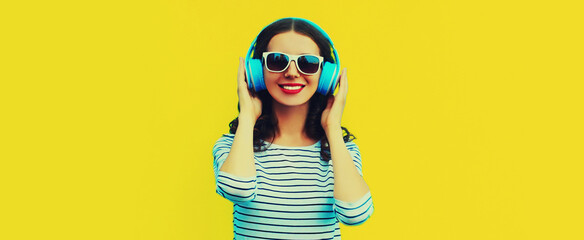 Portrait of happy smiling young woman with headphones listening to music on yellow background,...