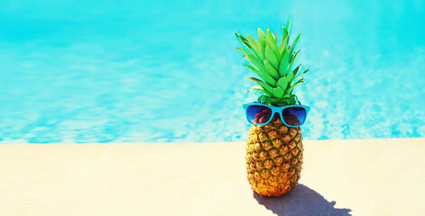 Funny pineapple with sunglasses on blue water pool background, summer holidays, vacation and food...
