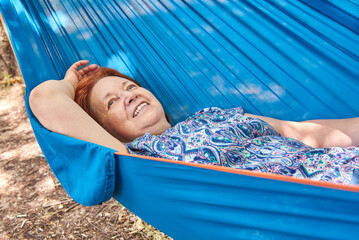 Hispanic mature woman on vacations smiling lying in a blue hammock.