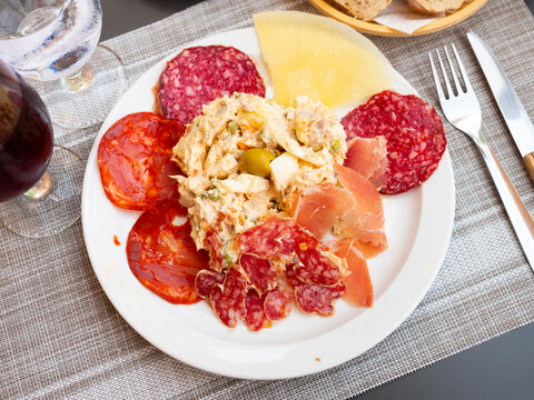Plate with coldcuts from sliced salami, fuet, chorizo, jamon iberico and hard cheese served with russain salad. Popular Spanish entremets