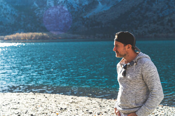 Man standing in front of mountain lake with ball cap on looking away 