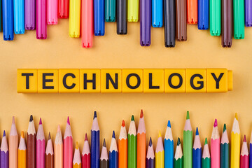 The word technology written on yellow cubes. Flat lay with colorful pencils. Devices concept.