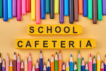 The inscription school cafeteria written on cubes. Colorful pencils and felt pens on table. Flat lay.