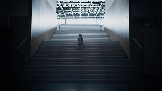 Lonely schoolchild sitting alone on school staircase closeup. Boy hide in hall.