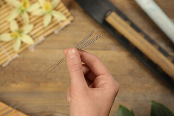 Woman holding many acupuncture needles over wooden table, closeup
