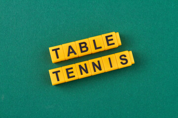 The inscription table tennis written on yellow cubes against green background. Flat lay.