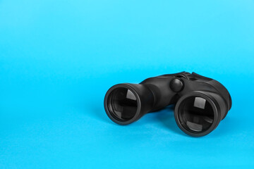 Modern binoculars on light blue background, space for text
