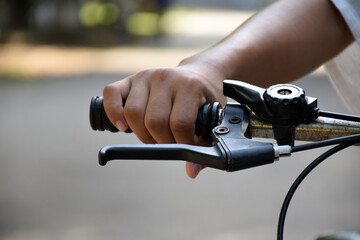 Closeup view of handlebar of bicycle which has hand of kid holding it, soft and selective focus.