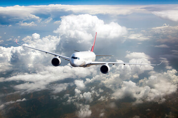Passenger plane flies high in the blue sky above the clouds. Front view. Right heeling.