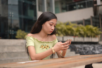 A disappointed young woman messages her no-show date while seated at an outdoor cafe at a mall...