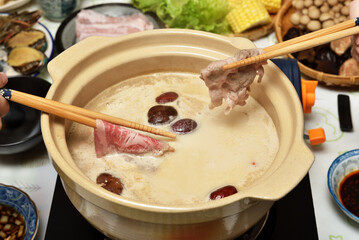 Two people use chopsticks to take meat slices from a hot pot