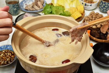Two people use chopsticks to take meat slices from a hot pot