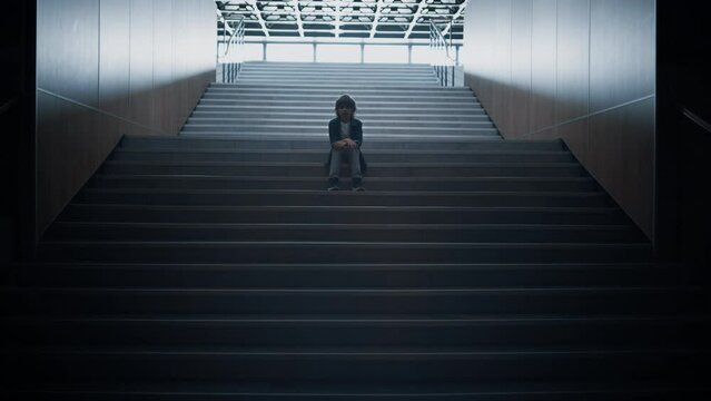 Unhappy schoolboy sitting staircase alone close up. Lonely bullies victim hiding