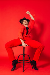 Fototapeta na wymiar Tall handsome man dressed in red shirt, trousers and black hat posing on the red background