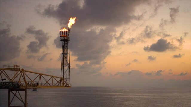 Slow motion of gas flare from bottom burning at oil and gas platform with background sun set and sea for oil and gas business concept.