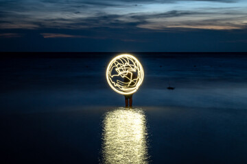 Figura luminosa en forma de planeta en playa al anochecer. Fotografía de larga exposición © Javier