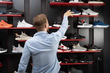 young man picking a sporty shoes in the shop, new sneakers in sports store for men, shopping sports...