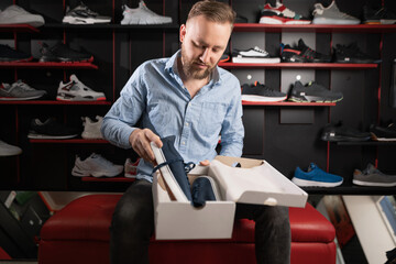 Young man trying on sports shoes in a sportswear store, choosing sneakers for men in a fitting room