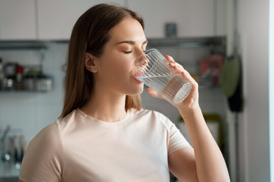 Thirsty young woman drinking fresh water from glass headshot portrait