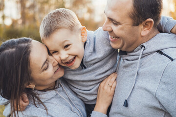 Fototapeta premium Happy parents and son are smiling together while standing in the park, posing in the daytime. The perfect little family. Family in nature.