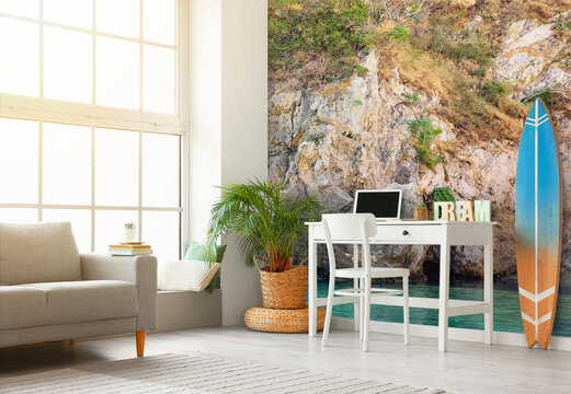 Comfortable sofa, workplace and surfboard in interior of room with photo wallpaper