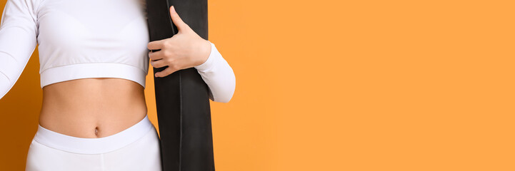 Sporty female coach holding yoga mat on orange background with space for text