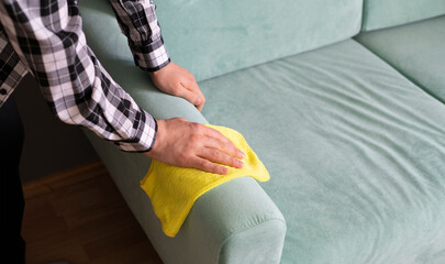 worker with yellow microfiber rag cleaning sofa textile at home