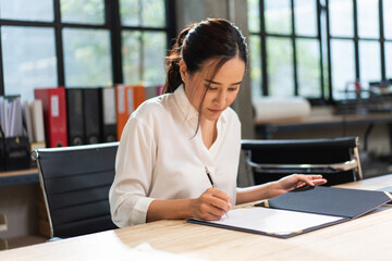 Asian business female project manager reading document report at desk in the office. work data and information. signing approve on business contract agreement.