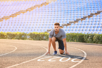 Sporty young man in crouch start position near figure 2022 on running track at the stadium