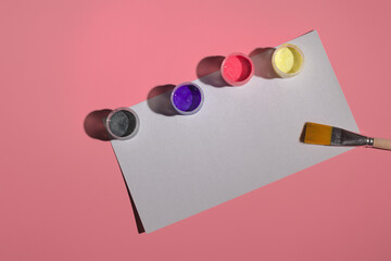 acrylic paint, brush and white sheet lie on a colored background, top view
