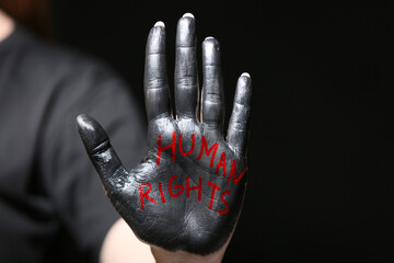 Woman with paint and text HUMAN RIGHTS on her palm against dark background, closeup