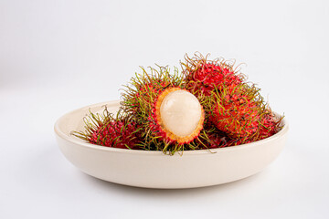 Rambutan fruit on ceramic white plate on white table background.