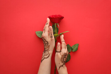 Female hands with beautiful henna tattoo and rose flower on color background, closeup