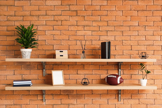Shelves with stylish decor and rugby ball on brick wall