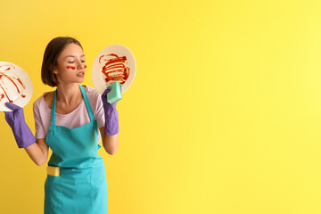 Young woman with cleaning sponge and dirty dishes on yellow background