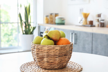 Wicker basket with fruits on dining table in kitchen, closeup